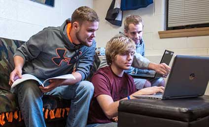 Three students in dorm room looking at laptop